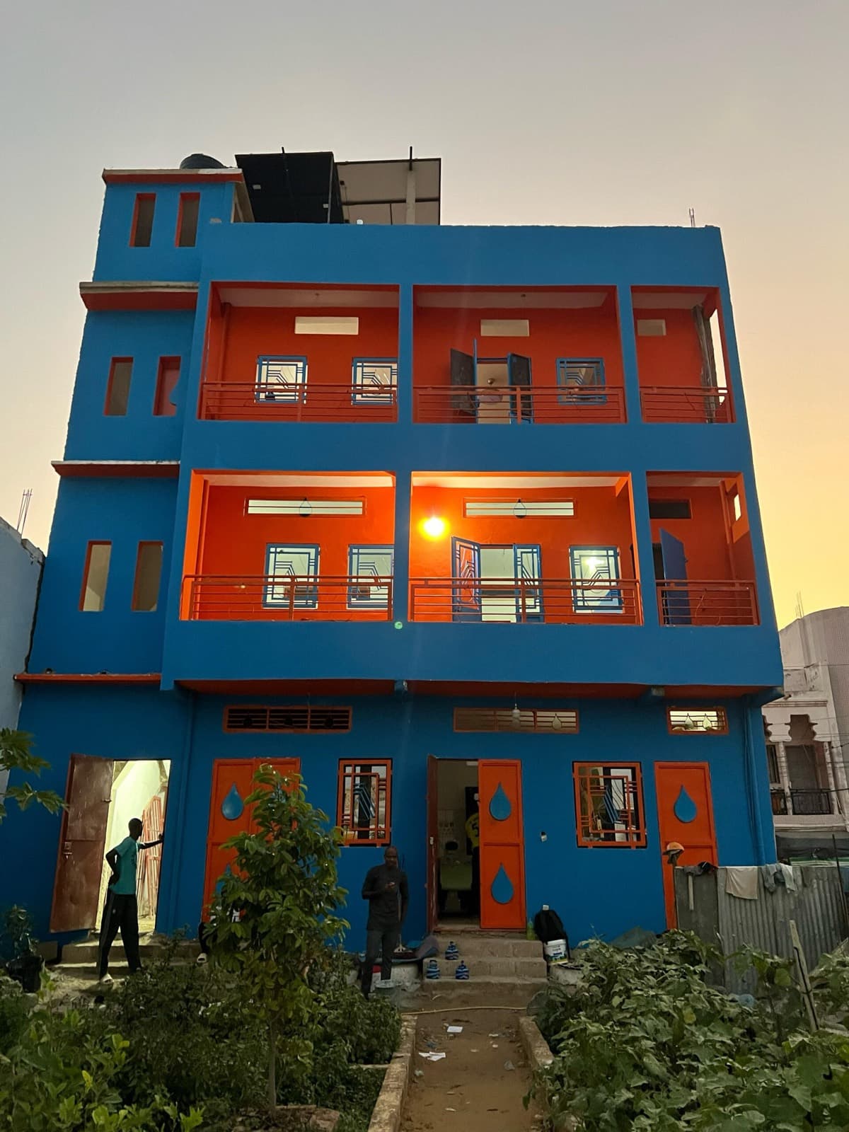 Un bâtiment scolaire de trois étages peint en bleu et orange, photographié au coucher du soleil.