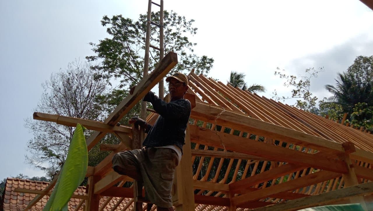 Un charpentier ajuste la structure en bois de la toiture d'une salle de classe en construction.