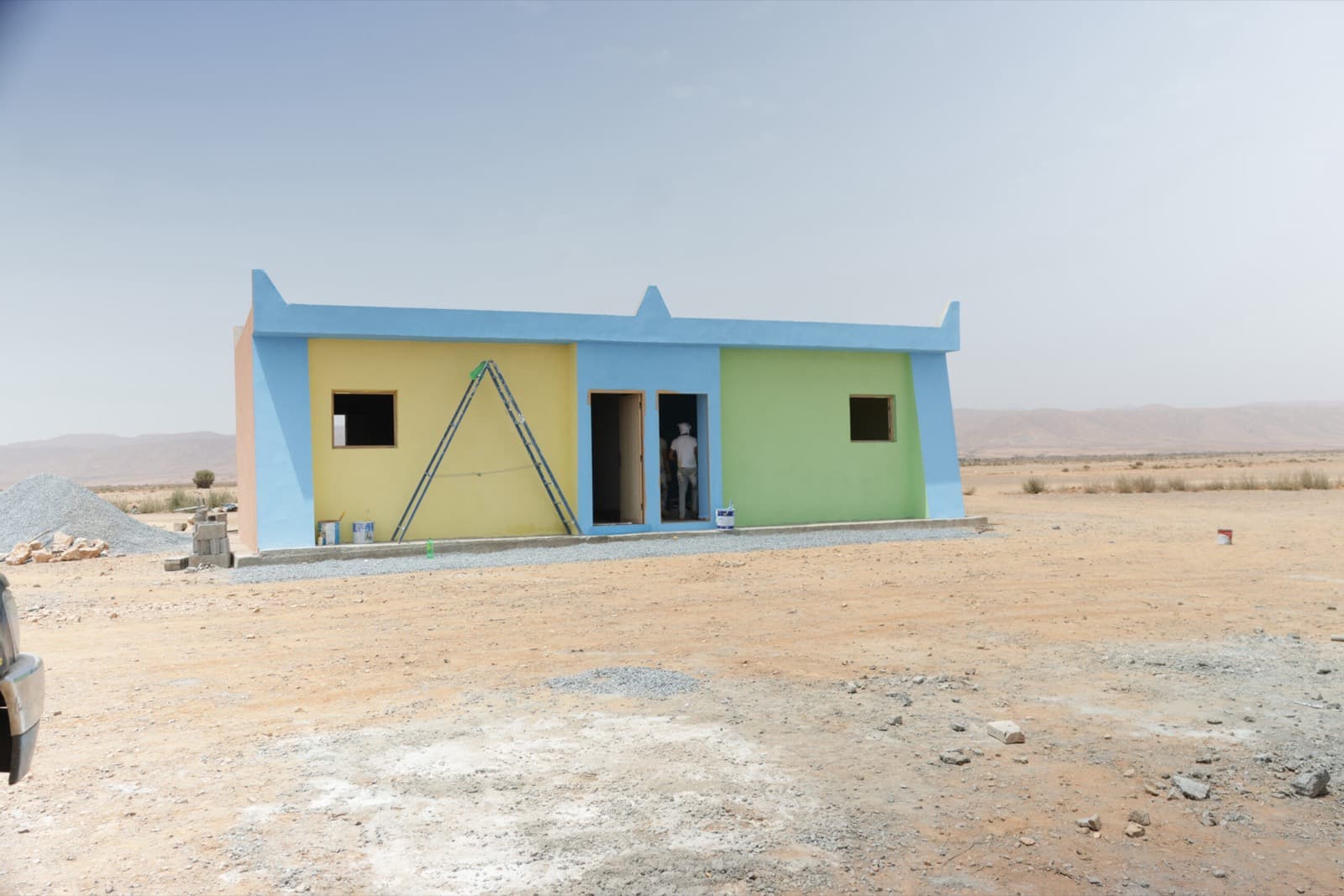 L'école terminée, façades jaune, bleue et verte, ouverte sur l'horizon du désert.
