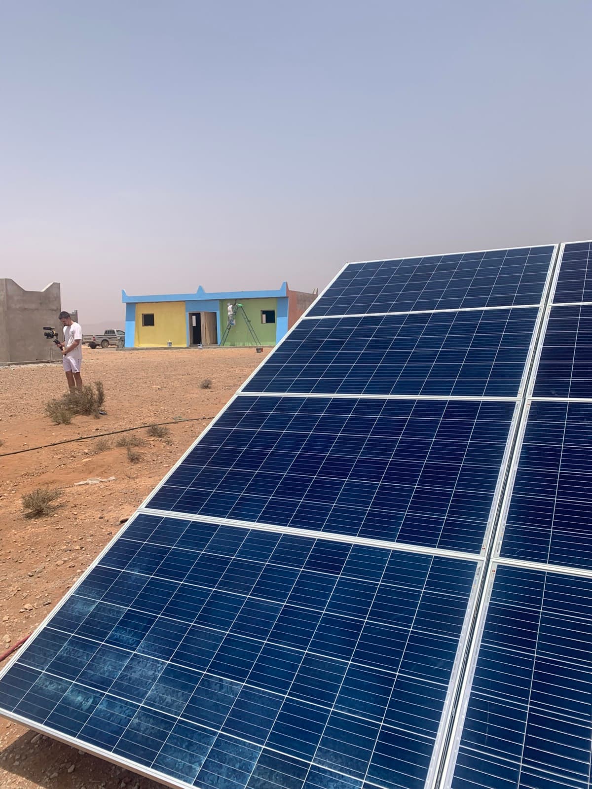 Une rangée de panneaux solaires posée au sol, face à l'école qu'elle alimente en électricité.