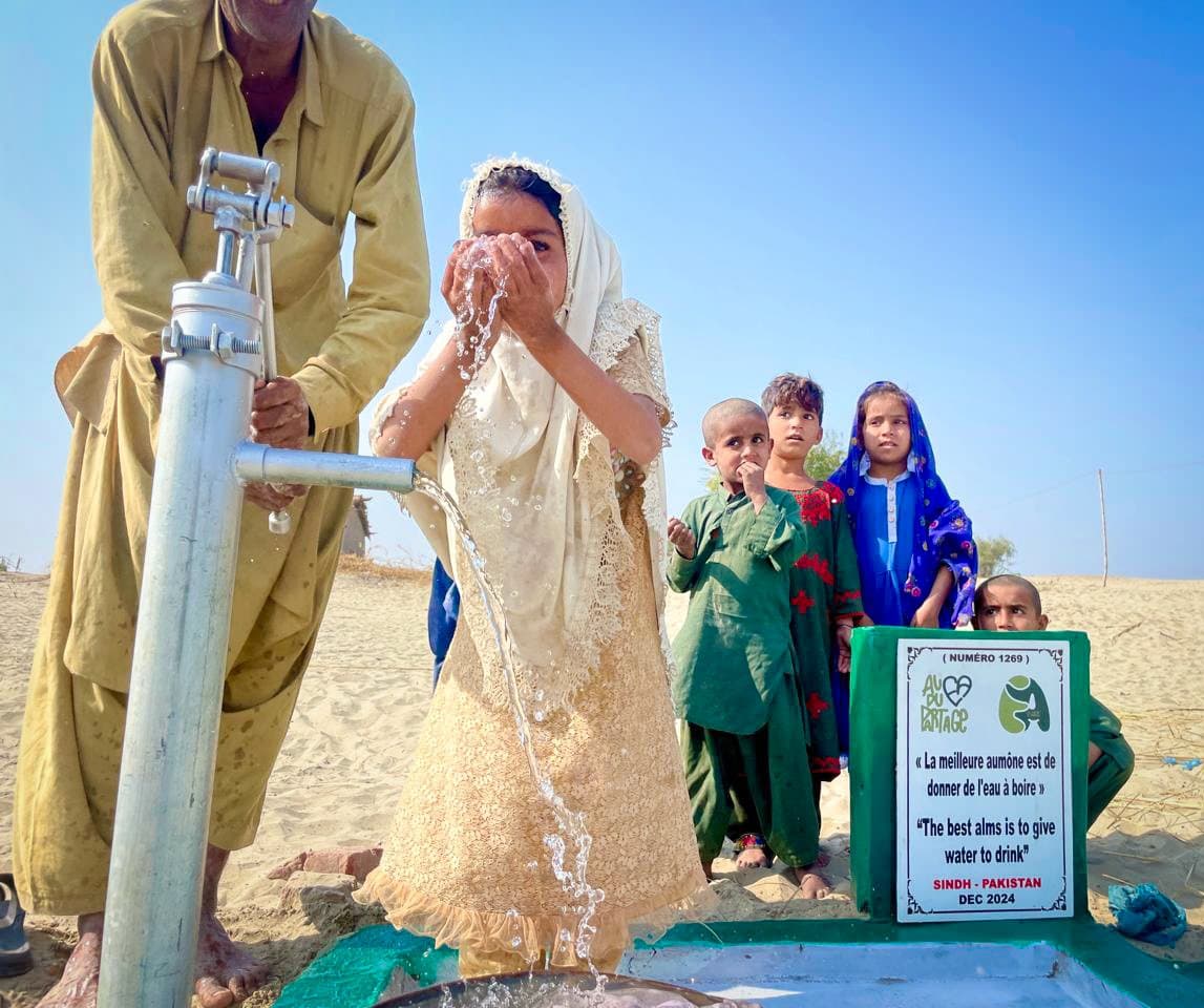 Une fillette sourit sous le jet d'eau claire d'un puits, entourée d'autres enfants du village.