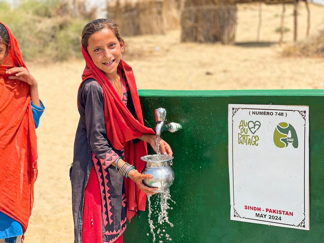 Au Pakistan, une fillette remplit un pot à l'un des robinets d'un puits construit par l'association.