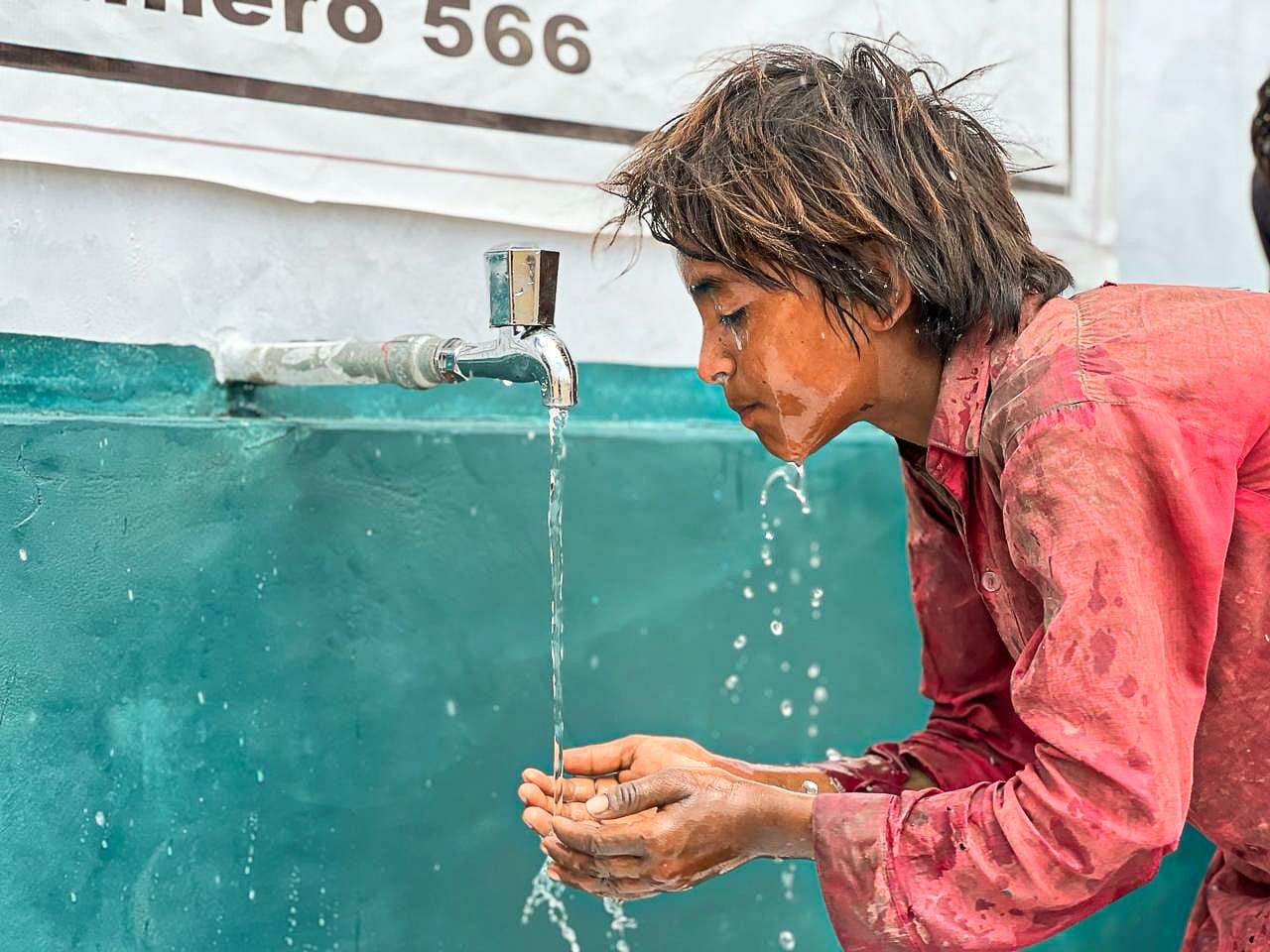 Un garçon boit l'eau dans le creux de ses mains, au robinet d'un puits au Pakistan.
