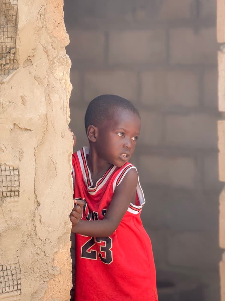 Un petit garçon en maillot de basket rouge regarde l'objectif, appuyé contre un mur.