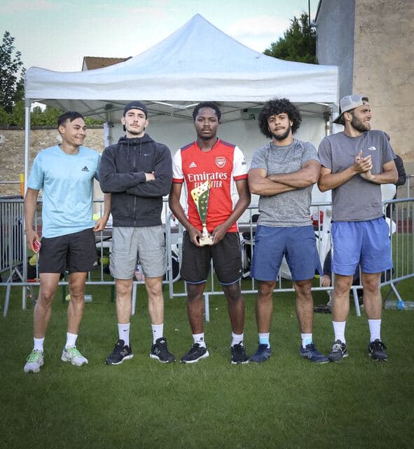 Cinq bénévoles en tenue de sport alignés devant un barnum blanc, l'un d'eux tient un trophée.