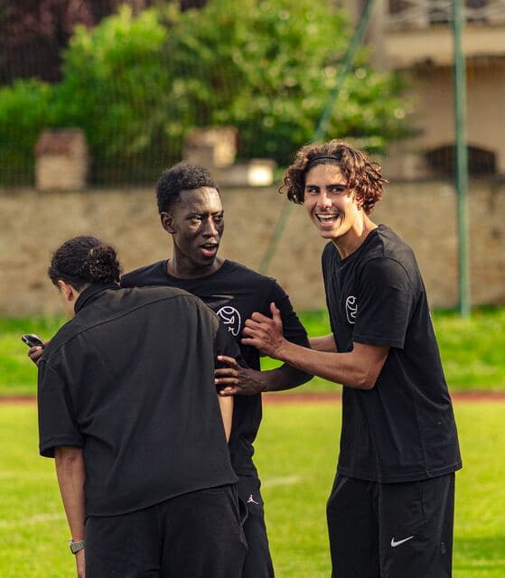 Trois bénévoles se saluent en riant sur la pelouse du terrain.