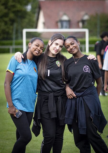 Trois bénévoles enlacées sourient au bord d'un terrain de football.