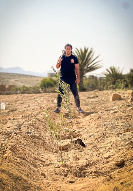 Un bénévole se tient au milieu d'un champ labouré, un jeune plant au premier plan.