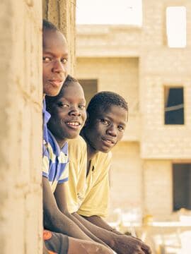 Trois enfants souriants apparaissent dans l'embrasure d'un bâtiment en construction.
