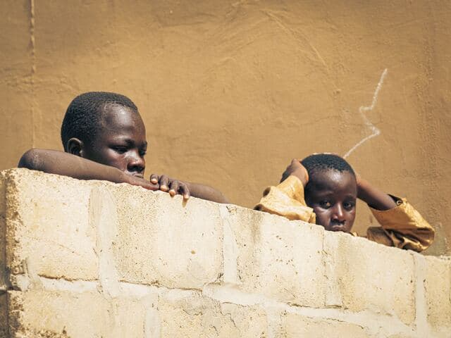 Deux enfants accoudés à un muret observent la scène.