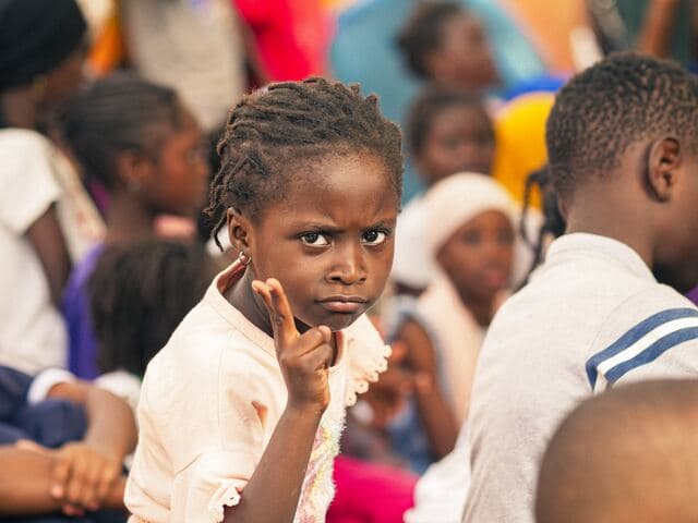 Une fillette lève la main au milieu d'une assemblée d'enfants assis.