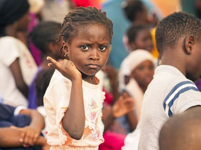 Une fillette au regard sérieux, au milieu du groupe d'enfants réunis.