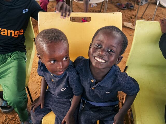 Deux petits garçons en polo bleu assis côte à côte sur des chaises d'école.