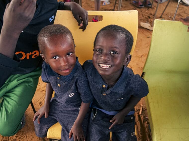 Deux petits garçons éclatent de rire, assis côte à côte sur des chaises d'école.