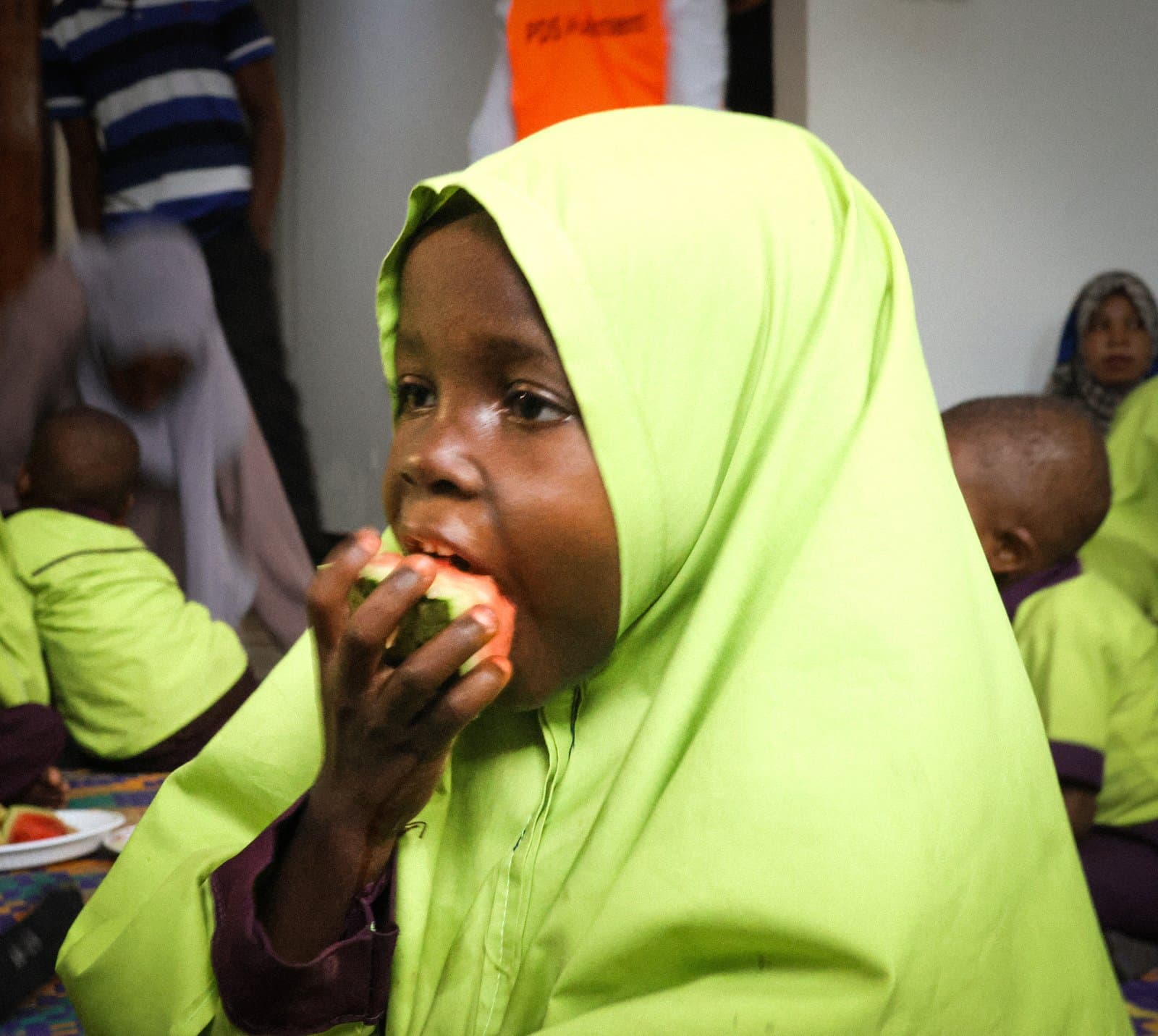 À Zanzibar, une fillette au voile vert croque dans son repas.