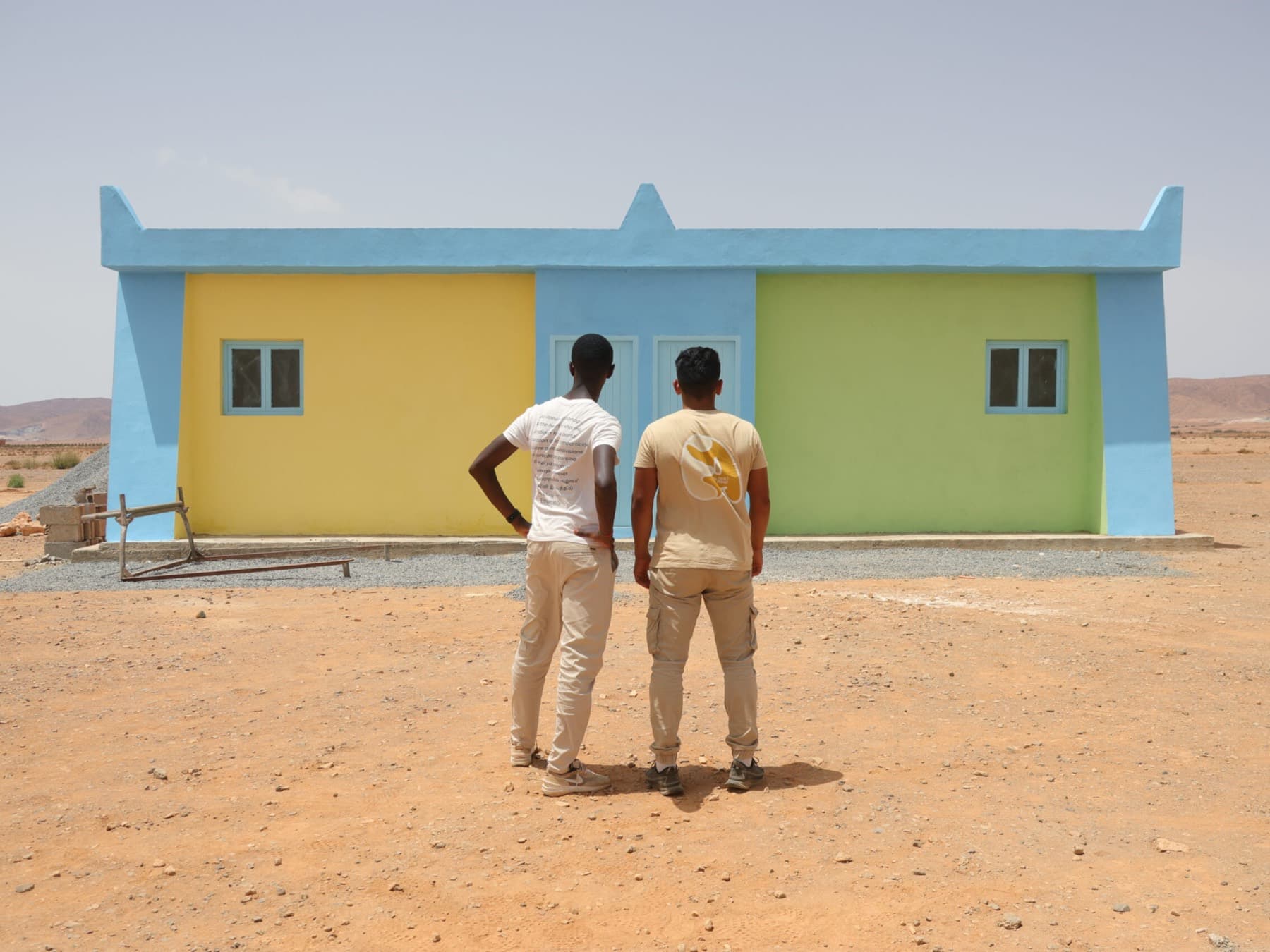 Deux bénévoles regardent l'école qu'ils viennent de repeindre, seule construction du désert alentour.