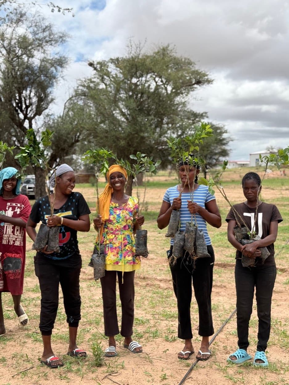 Un groupe de femmes souriantes tient chacune un jeune arbre fruitier avant la plantation.