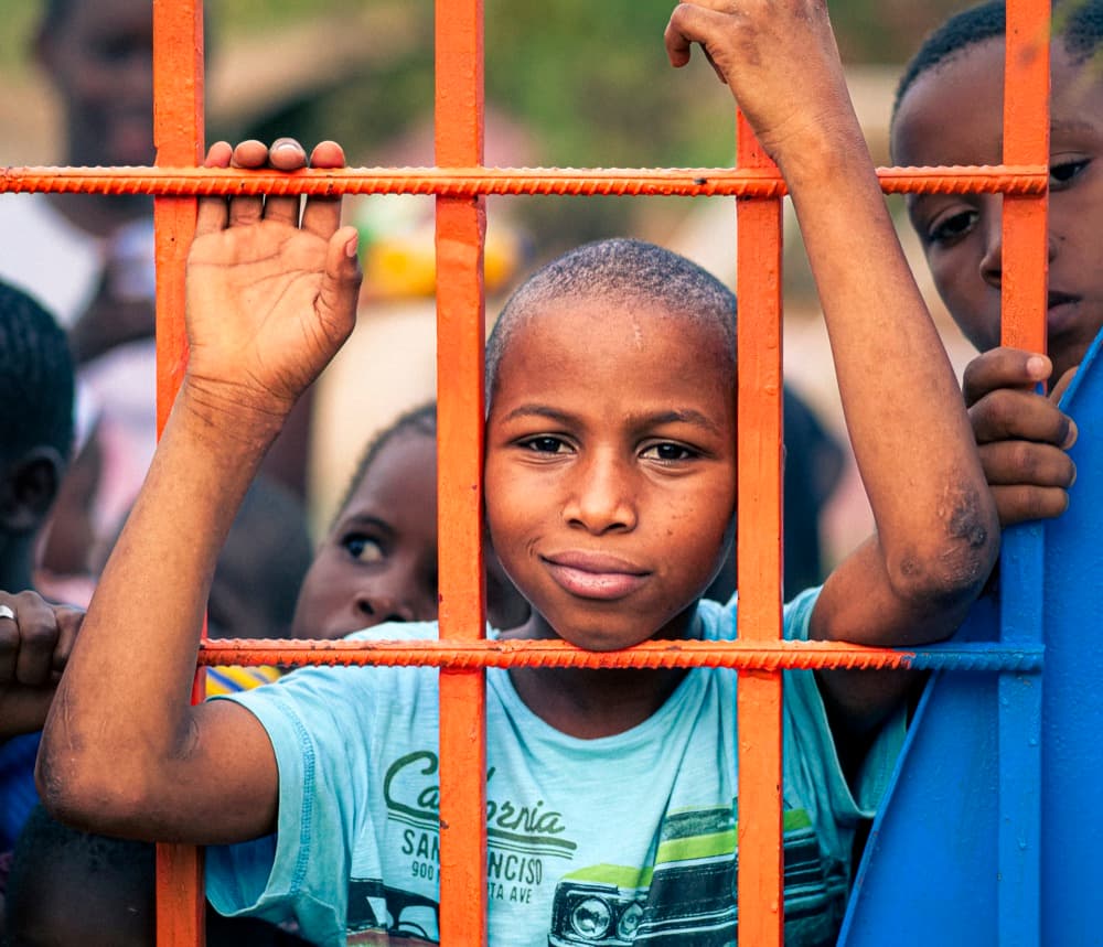 Un enfant souriant s'appuie au portail orange de l'école.