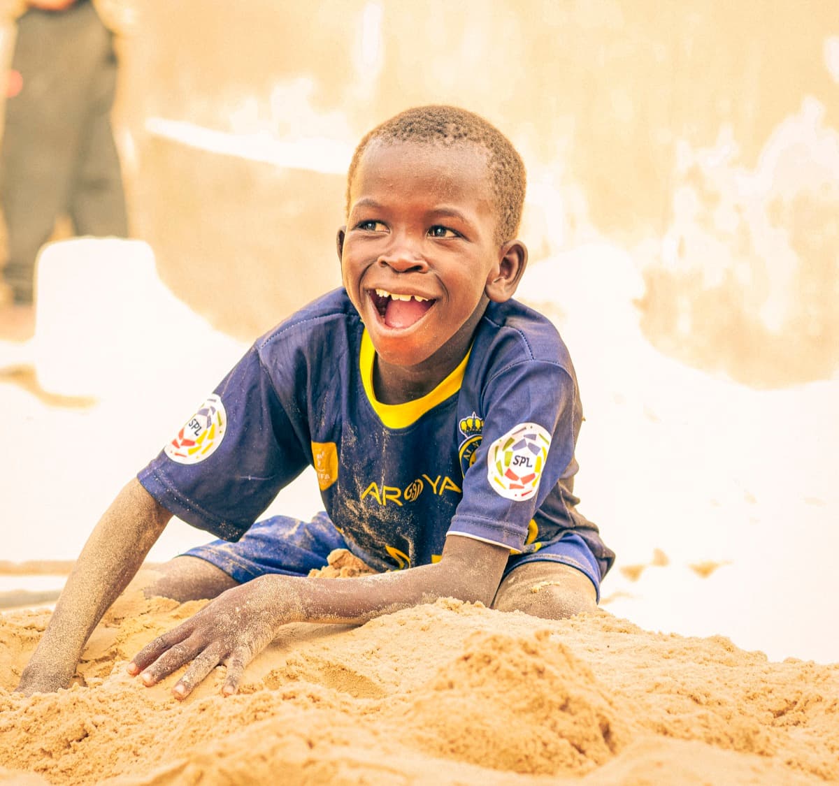 Un enfant rit en jouant dans le sable devant l'école.