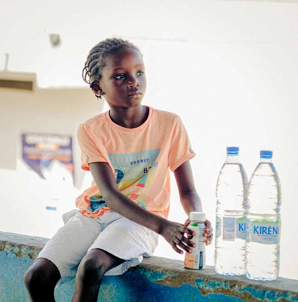 Une fillette assise avec des bouteilles d'eau lors d'une distribution.