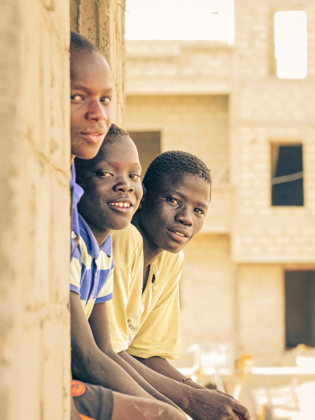 Trois garçons souriants assis à l'ouverture d'une fenêtre du centre en construction.