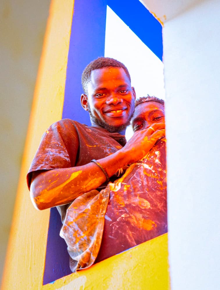 Deux jeunes peintres sourient à la fenêtre du bâtiment qu'ils rénovent.