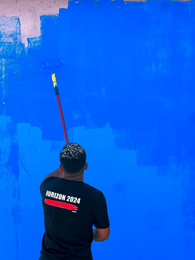 Un bénévole repeint en bleu le mur d'une école.